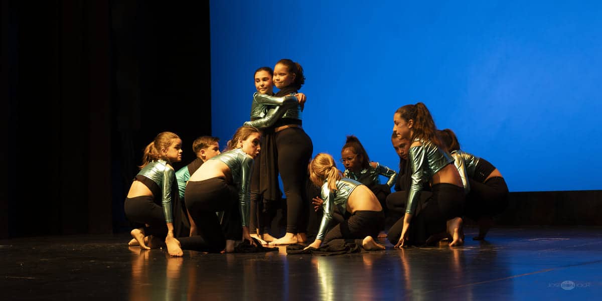Grupo de bailarinas adolescentes de Bailalé Huesca realizando una coreografía de estilo contemporáneo en el escenario con un fondo azul.